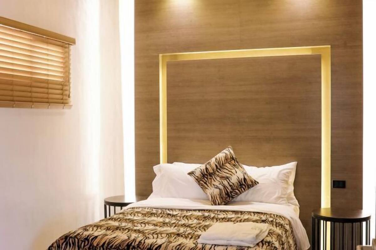 Un dormitorio moderno con cama, cabecera, mesitas de noche y ventana con persianas.
