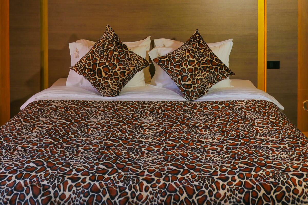 Una cama con colcha estampada, dos almohadas de estampado de leopardo y un cabecero con detalles decorativos.