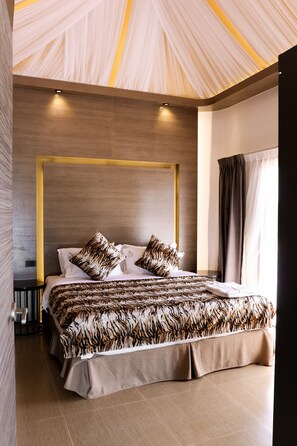 A modern bedroom with a large bed, a wooden headboard, and a ceiling with a unique light fixture. - Safari Hotel and Villas powered by Cocotel  (Vigan)
