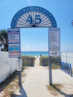A beach entrance with a sign indicating 'No Lifeguard on Duty' and 'Swim at Your Own Risk'.