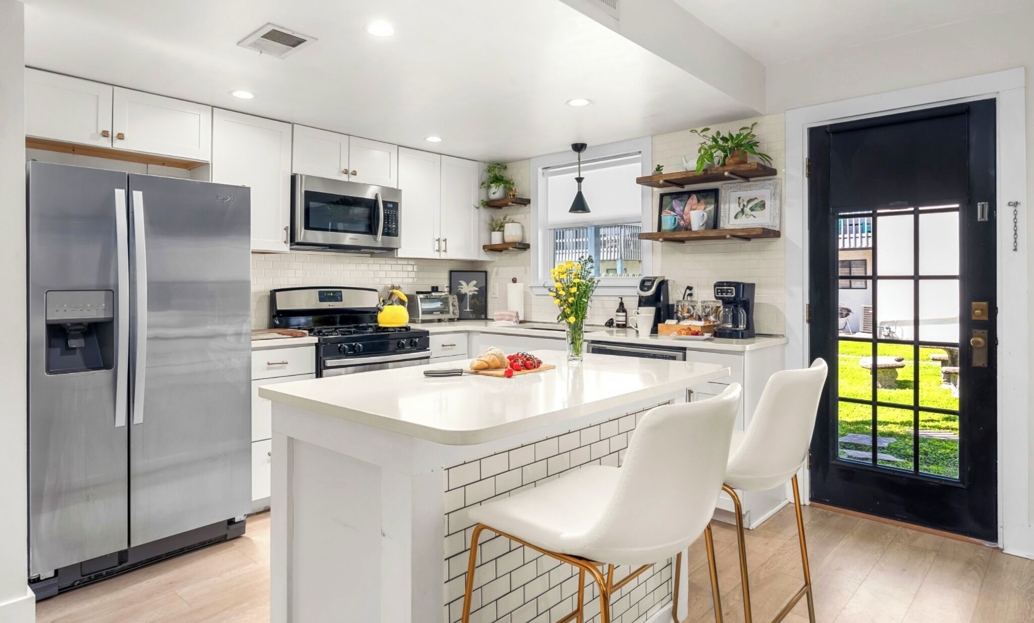 Una cocina moderna con armarios blancos, electrodomésticos de acero inoxidable y una isla central con taburetes de bar.