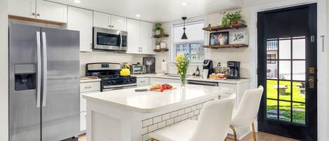 Una cocina moderna con armarios blancos, electrodomésticos de acero inoxidable y una isla central con taburetes de bar.