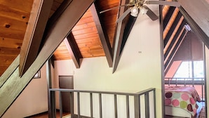 Camera mansardata con soffitto in legno, un balcone con ringhiera e un letto con copripiumino a pois.