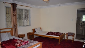 A bedroom with two single beds, a wooden nightstand, a small table, and a red patterned carpet.