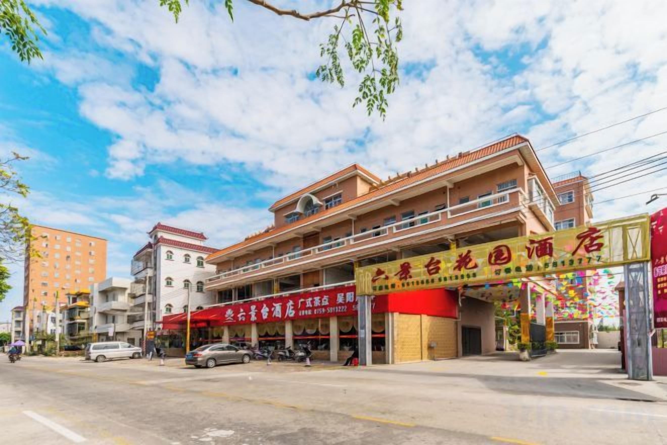 A multi-story building with a prominent red sign, a ground-level entrance, and a visible parking area.