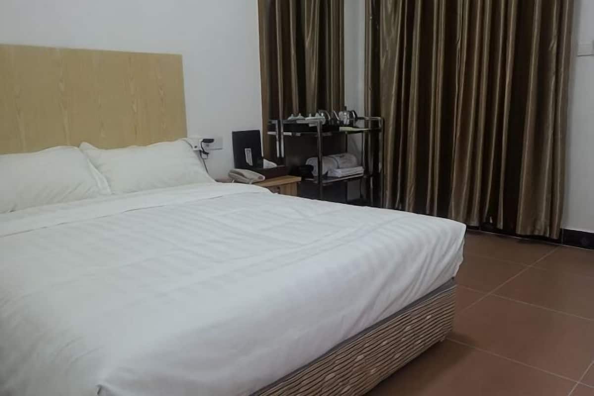 A hotel room with a large bed, a desk with a phone, and a wardrobe.