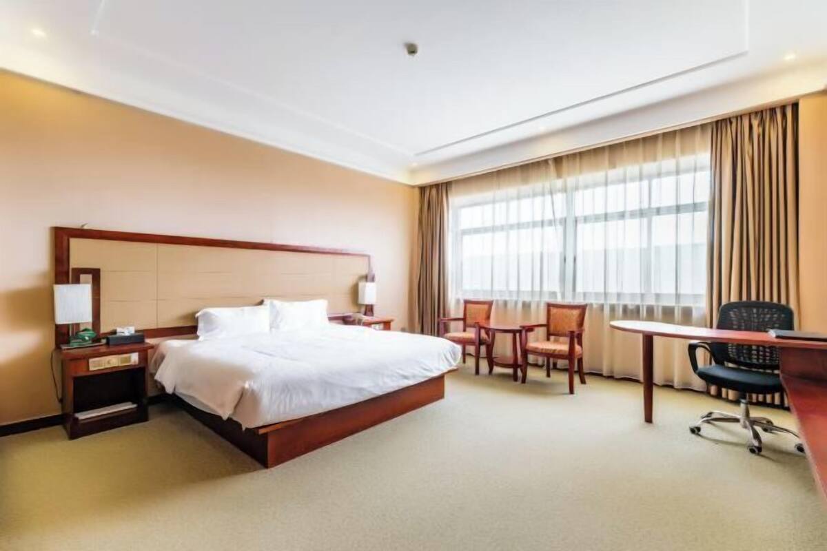 Een hotelkamer met een groot bed, een bureau, twee stoelen en een raam met gordijnen.