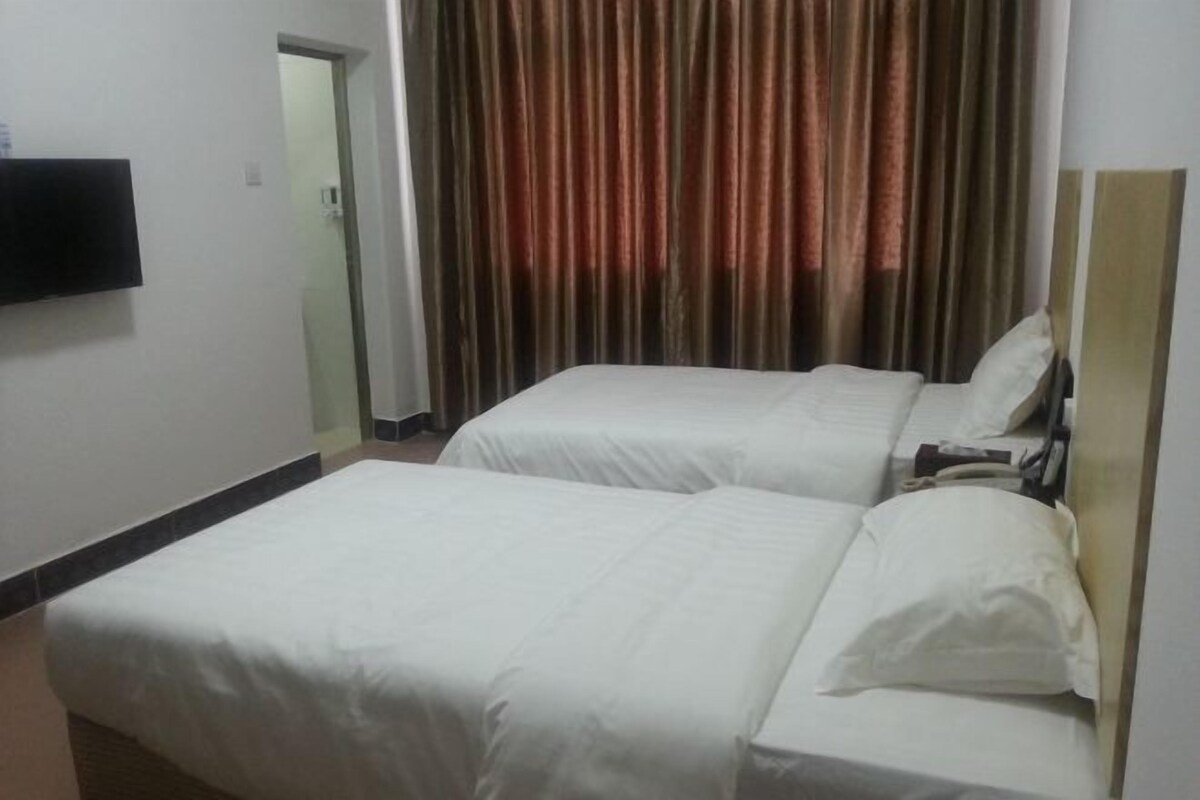 A hotel room with two beds, a flat-screen TV mounted on the wall, and a curtain with a brown and red pattern.