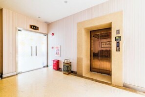 A hotel lobby with a reception desk, a door with a sign, an elevator, and a trash bin. - Liujingtai Garden Hostel (Wuchuan)