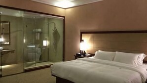 A hotel room with a bed, a nightstand, a lamp, a glass-enclosed shower, and a mirror. - Liujingtai Garden Hostel (Wuchuan)