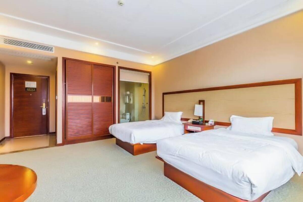 Een hotelkamer met twee bedden, een houten hoofdbord, een nachtkastje met een lamp en een deur met een bordje.