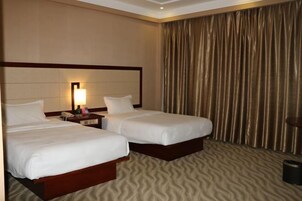 Habitación de hotel con dos camas, una mesita de noche con lámpara y un ventanal con cortinas.