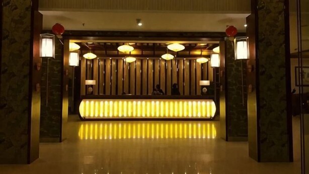 A reception area with a bright, illuminated counter, a wooden panel wall, and two wall-mounted lamps. - Liujingtai Garden Hostel (Wuchuan)