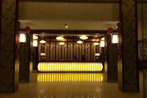 Un área de recepción con un mostrador luminoso e iluminado, un panel de pared de madera y dos lámparas fijadas a la pared.