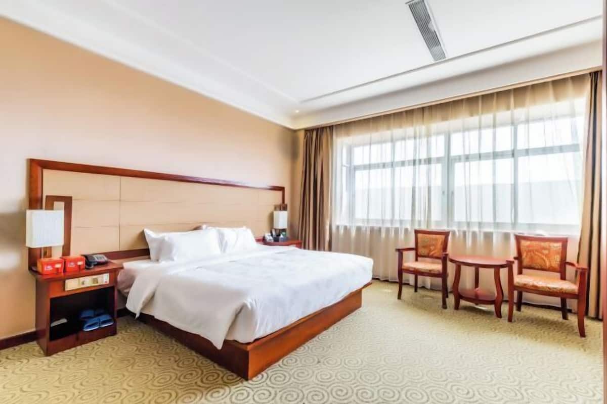 Hotelkamer met een groot bed, nachtkastje met lamp, stoel en raam met gordijnen.