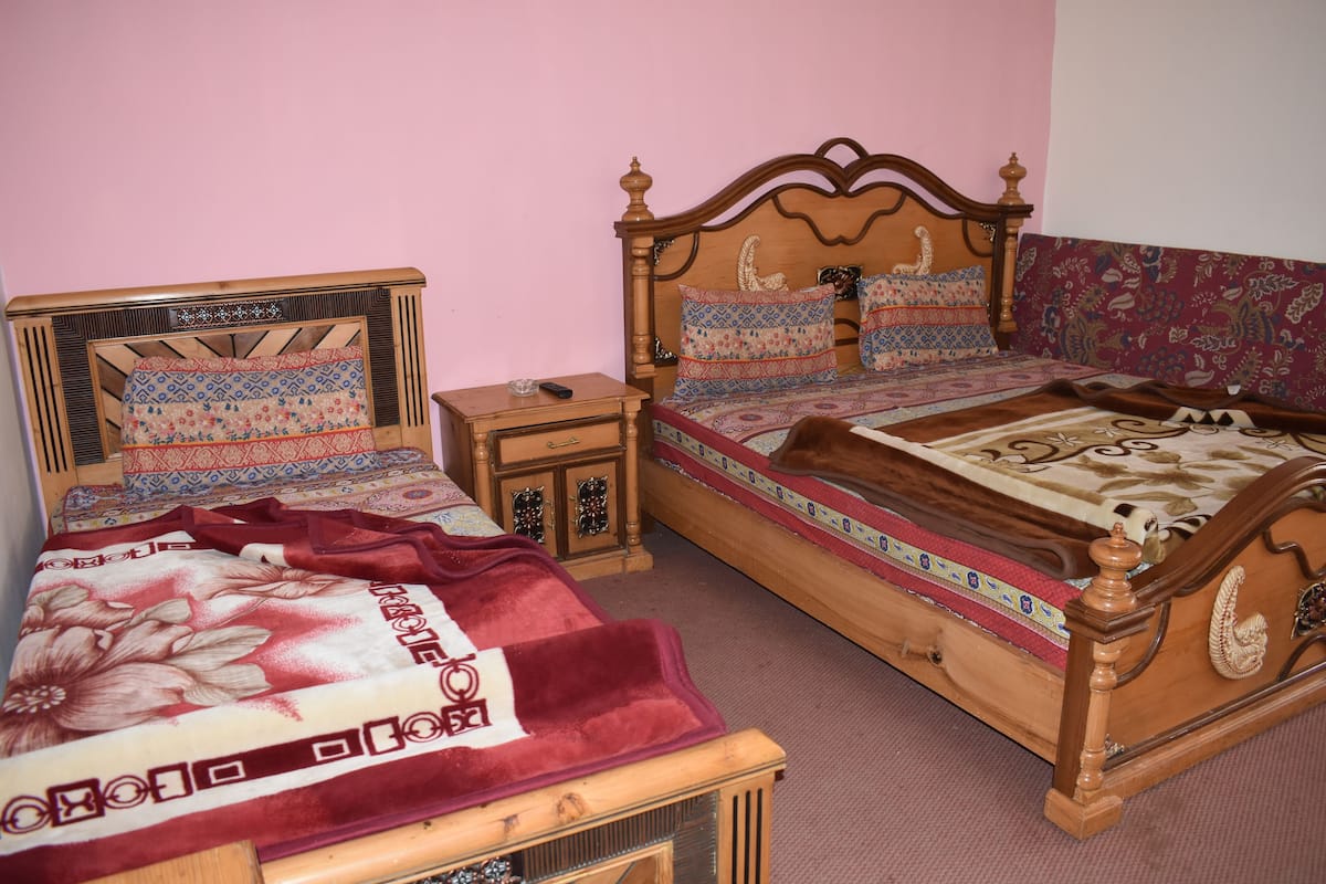 A bedroom with two wooden beds, each with patterned bedding and headboards. There is a nightstand with a lamp and a small drawer.