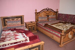 A bedroom with two wooden beds, each with patterned bedding and headboards. There is a nightstand with a lamp and a small drawer.