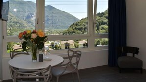 A room with a large window overlooking a mountainous landscape, a dining table with chairs, and a TV mounted on the wall. - Capriccio 16 Pergola by Interhome (Intragna)