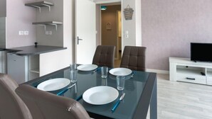 Un comedor moderno con una mesa de vidrio dispuesta para cuatro personas, dos sillas de cuero marrón, un armario blanco con televisor de pantalla plana y una puerta que conduce a otra habitación.