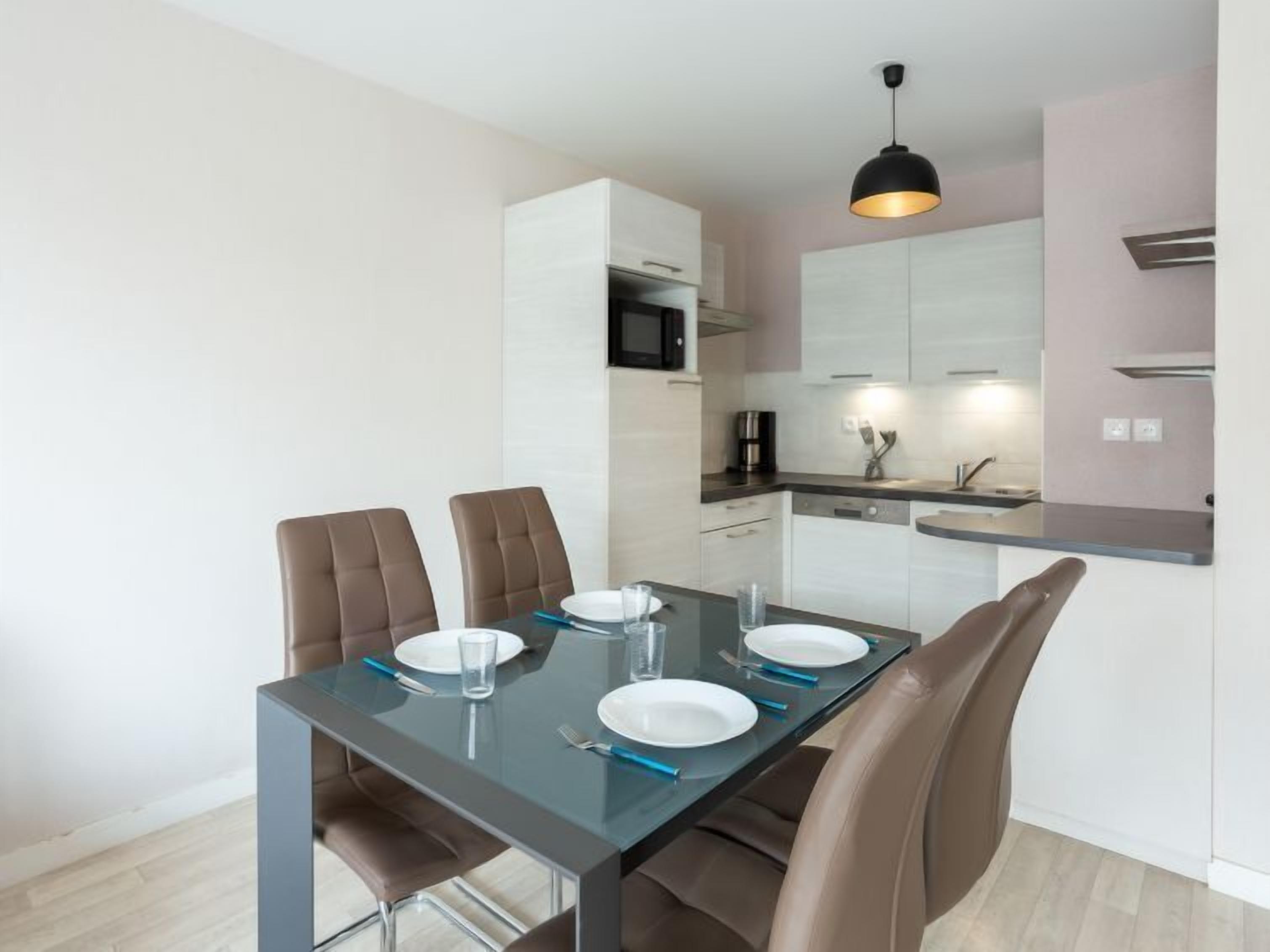 Un comedor moderno con una mesa de vidrio, cuatro sillas marrones y una lámpara colgante negra.