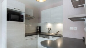 Una cocina compacta con armarios blancos, un microondas negro, un lavamanos de acero inoxidable y una cafetera.
