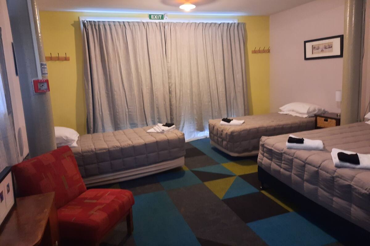 A hotel room with two beds, a red armchair, and a colorful carpet.