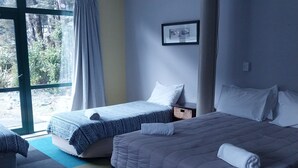 A hotel room with two beds, a large window, and a view of greenery outside.