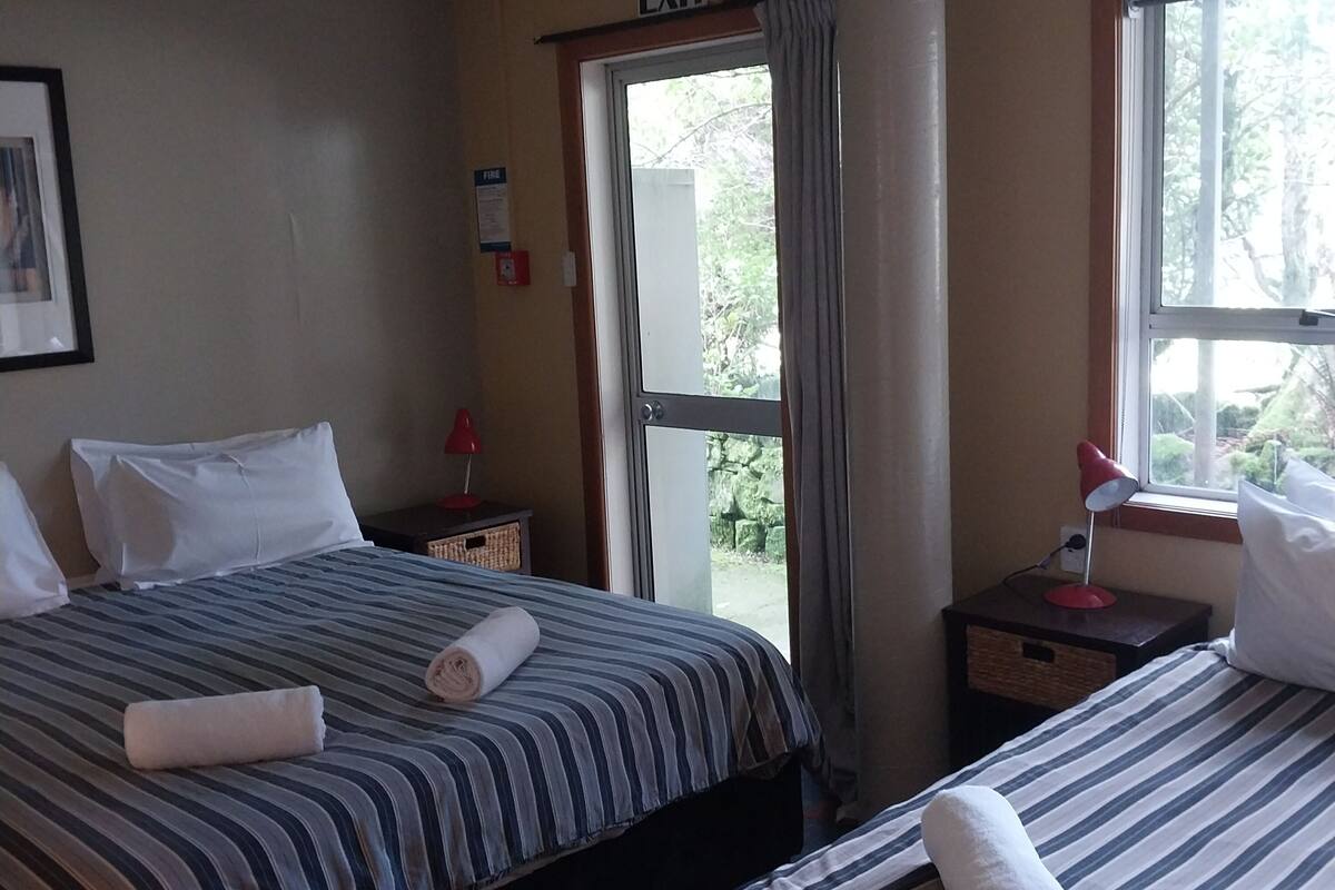A hotel room with two beds, a window, a door, and an exit sign.