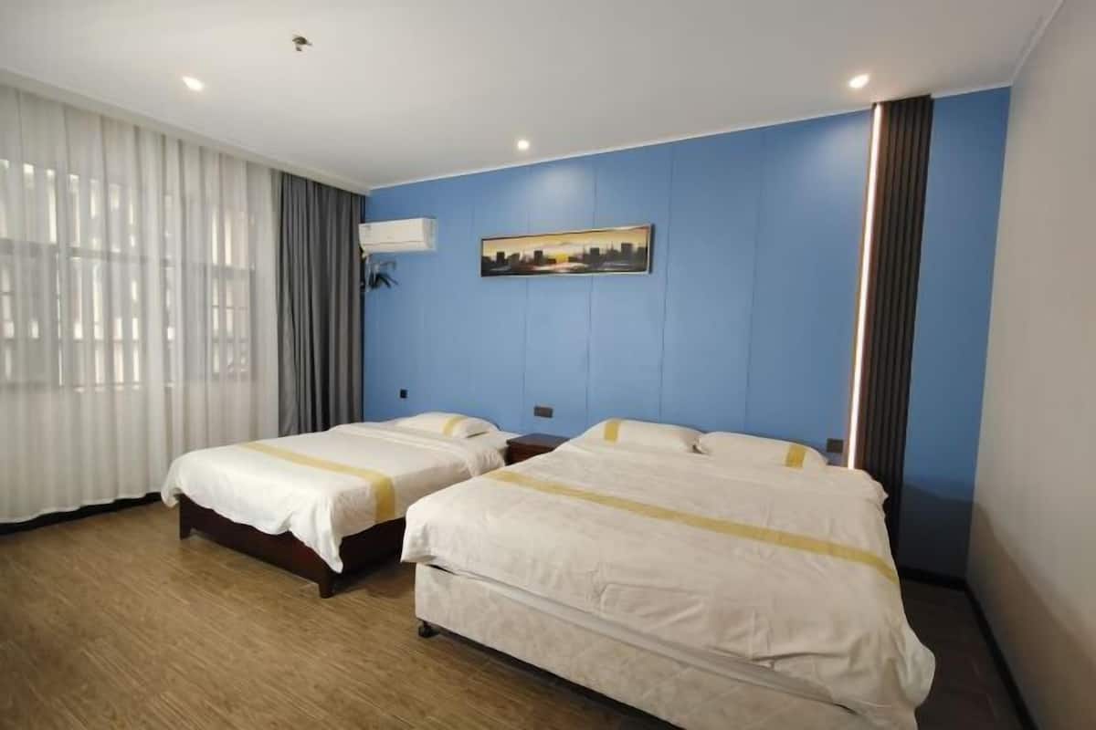 Quarto de hotel com duas camas, uma janela grande com cortinas, um quadro na parede e uma luminária no teto.