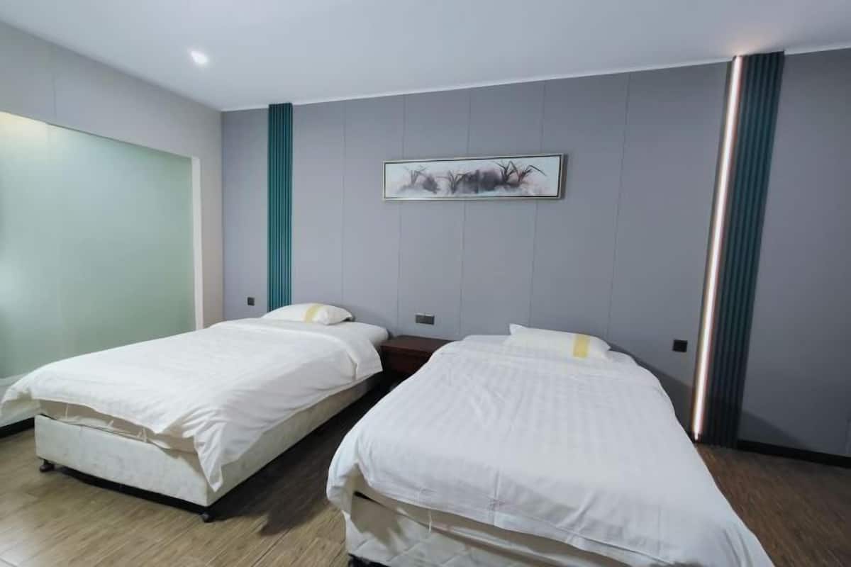 Quarto de hotel com duas camas de solteiro, uma janela grande e uma obra de arte pendurada na parede.