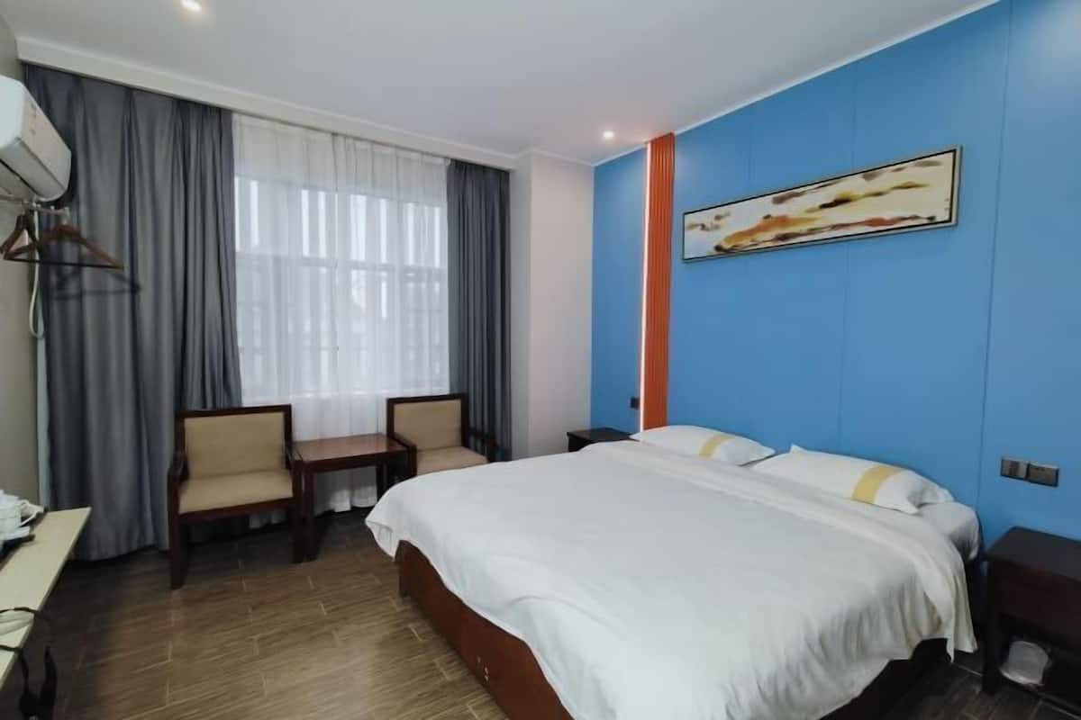 Quarto de hotel com uma cama grande, uma escrivaninha, duas cadeiras, uma mesa pequena e um quadro na parede.