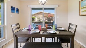 A dining area with a table set for four, a chandelier, and a window with a view of a house and garden. - Heated Pool, Tiki Hut, Game Room, Beach Gear, BBQ! (Cocoa Beach)