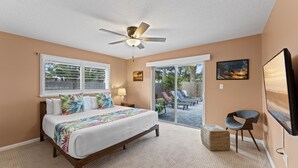 A bedroom with a bed, a ceiling fan, a window, a door leading to an outdoor area, and a TV mounted on the wall. - Heated Pool, Tiki Hut, Game Room, Beach Gear, BBQ! (Cocoa Beach)