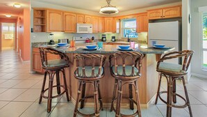 A kitchen with wooden cabinets, a central island with stools, a refrigerator, and a microwave. - Heated Pool, Tiki Hut, Game Room, Beach Gear, BBQ! (Cocoa Beach)