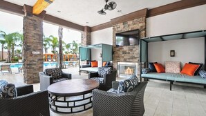 Een terras met een loungehoek, rieten meubels, een ronde tafel, een tv die aan een stenen muur is bevestigd, en een open haard.