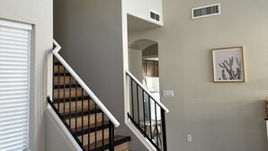 Una escalera con escalones de madera y barandillas negras, que lleva a un rellano con techo blanco y una rejilla de ventilación.