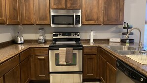 Una cocina con armarios de madera, estufa de acero inoxidable, microondas, tostadora, licuadora y lavavajillas.
