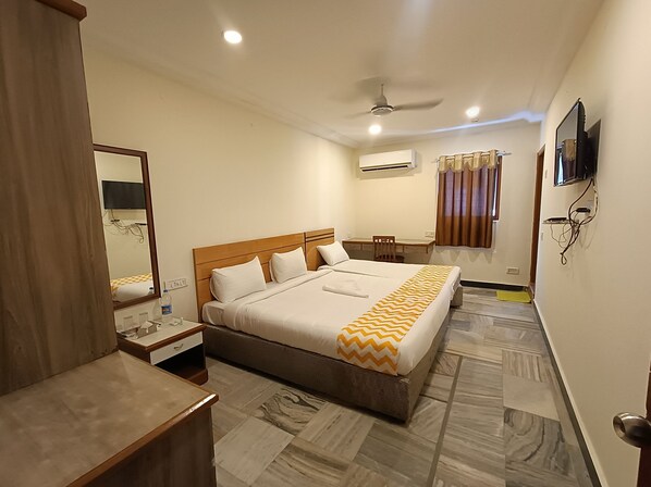 Habitación de hotel con cama, escritorio, silla, televisor y aire acondicionado.