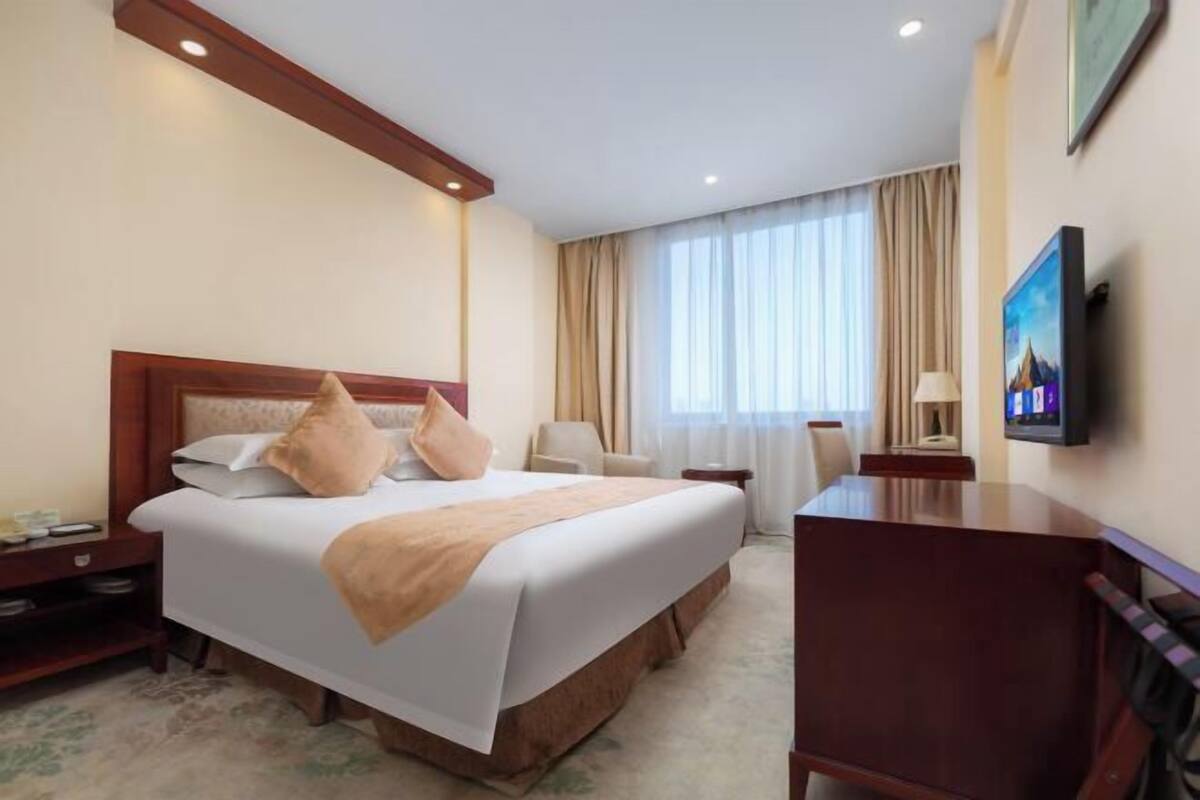 A hotel room with a large bed, a desk, a chair, a TV, and a window with curtains.