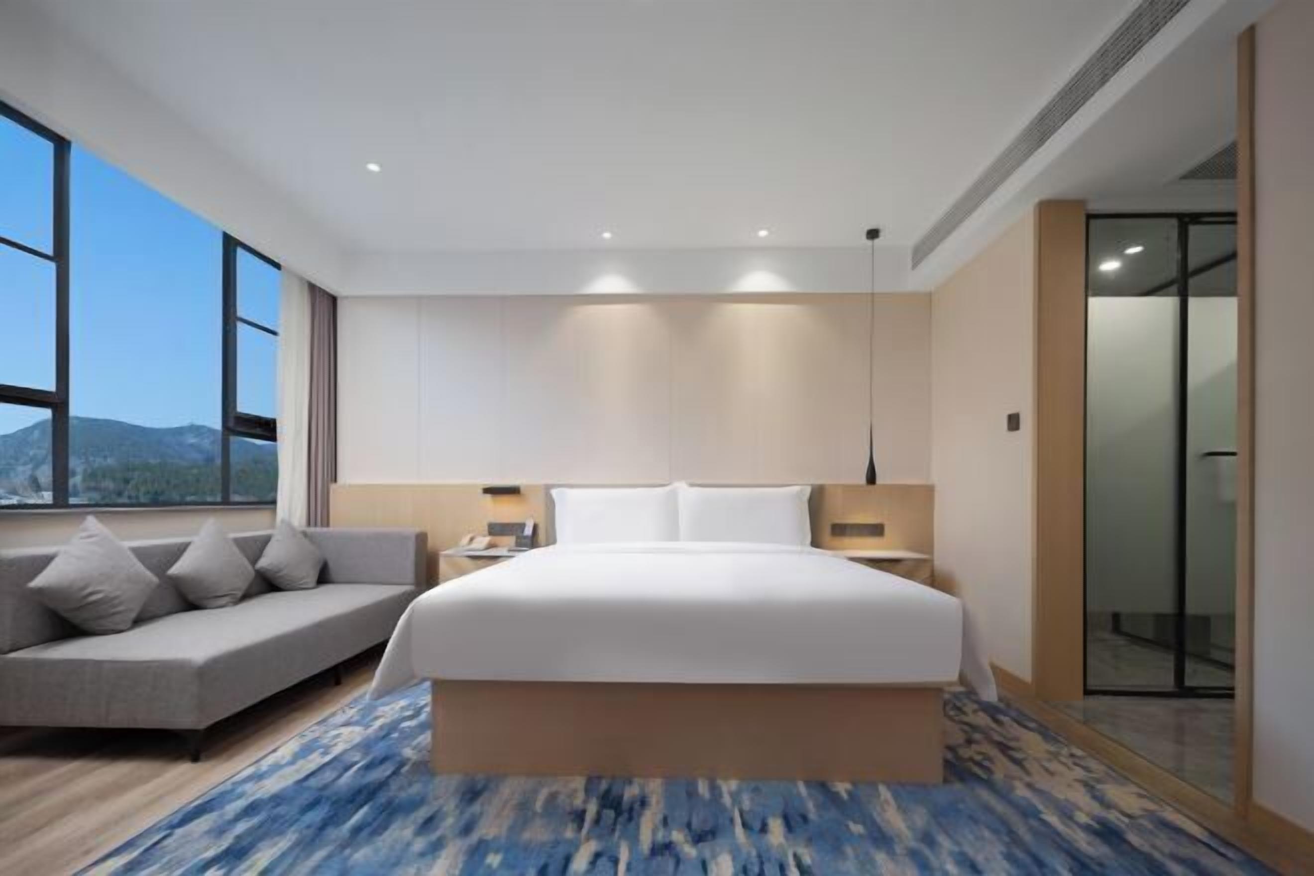 A modern hotel room with a large bed, a sofa, and a view of the mountains.