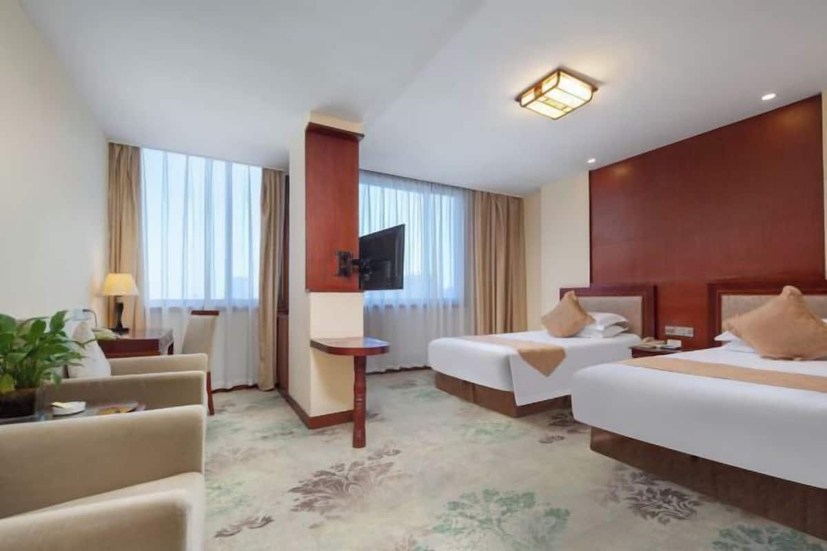 A hotel room with two beds, a TV, a desk, and a chair.