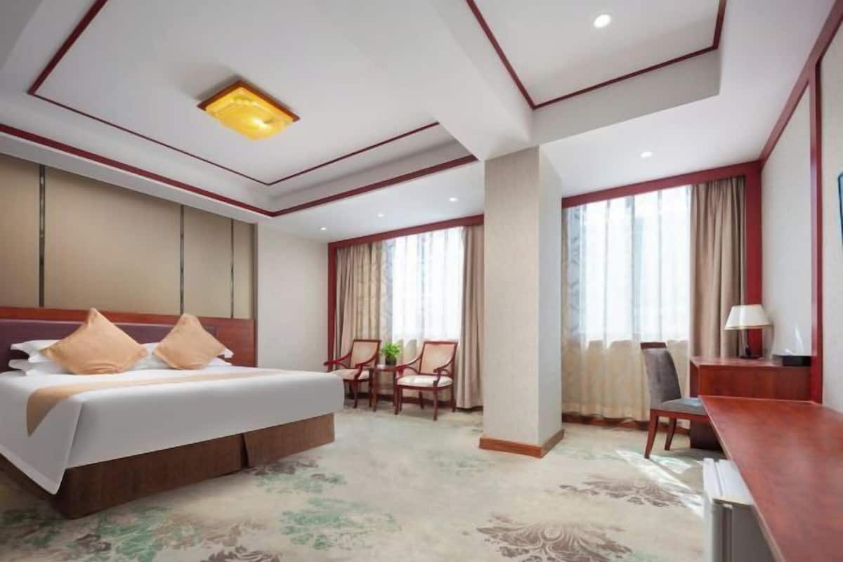 A hotel room with a bed, two chairs, a desk, and a large window with curtains.