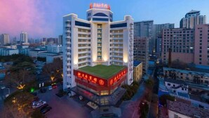 Un hotel de varios pisos con jardín en la azotea y letreros iluminados.