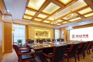 Un salón de conferencias con una larga mesa, varias sillas y una pantalla grande mostrando la marca del hotel.