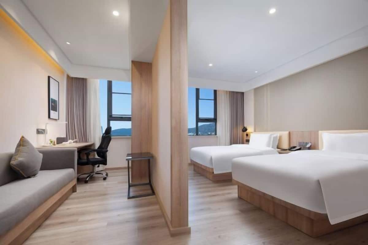 A hotel room with a sofa, two beds, a desk, and a chair.