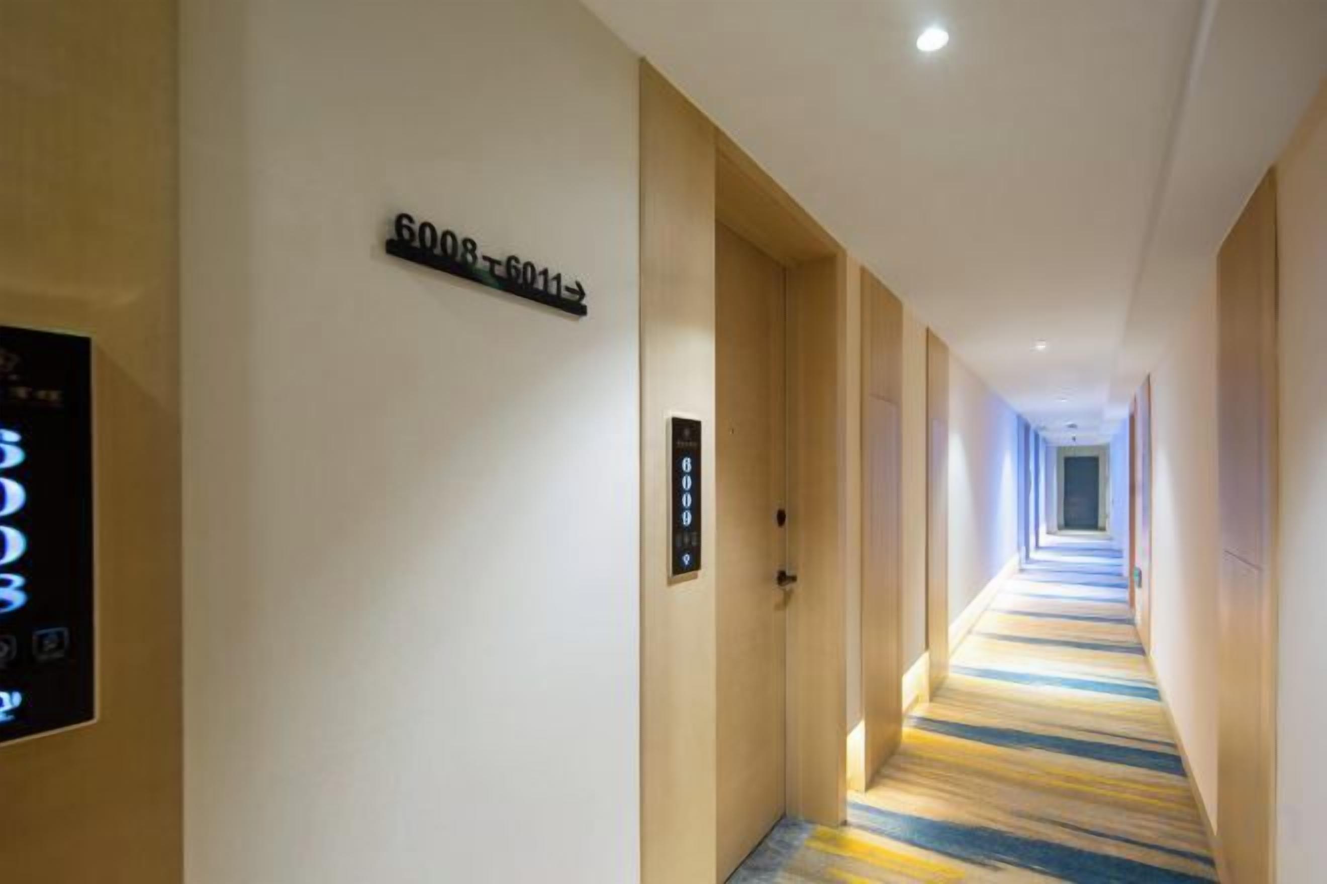 A hotel corridor with a carpeted floor, a digital display, and a door with a number sign.