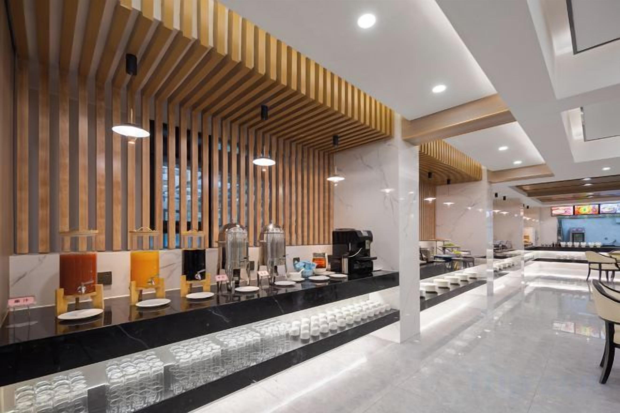A modern hotel lobby with a long reception desk, wooden slatted ceiling, and a seating area with tables and chairs.