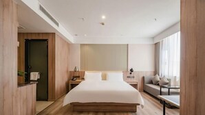 Una habitación de hotel moderna con una cama grande, suelo de madera, un sofá, un escritorio y una ventana con cortinas.
