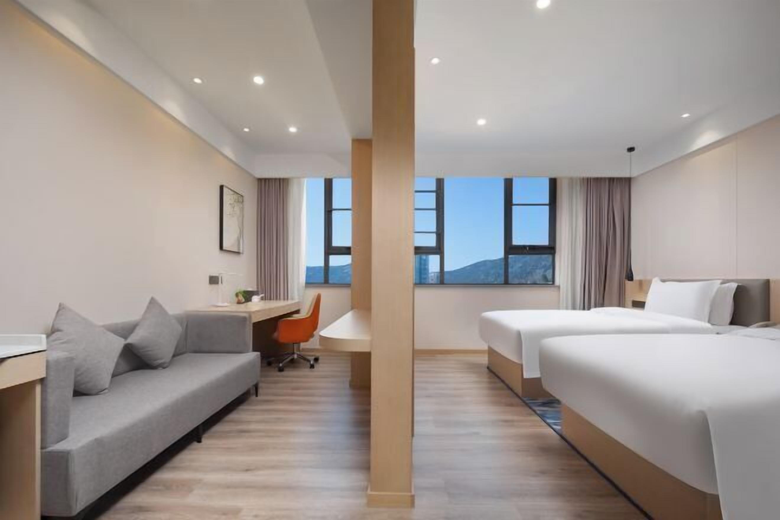 A hotel room with a sofa, two beds, a desk, and a chair.