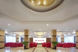 Un amplio salón con un escenario frontal, asientos rojos y candelabros.